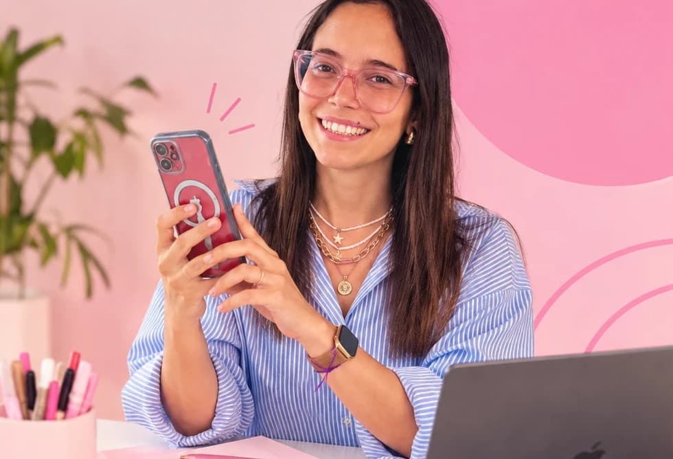 Juli sonriendo con el celular en la mano, frente a una pared rosa