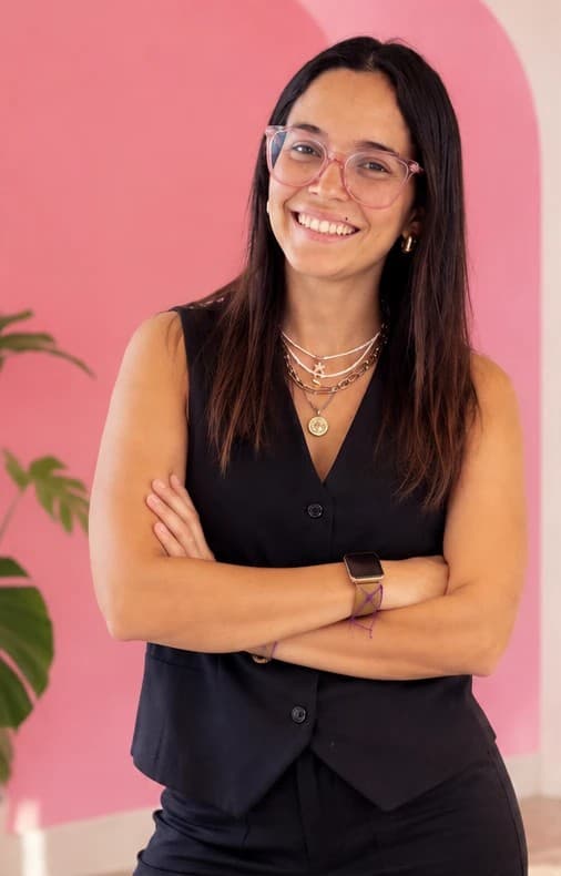Juli de brazos cruzados, sonriendo frente a una pared rosa